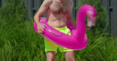 Neşeli bir adam flamingo şeklindeki şişirilebilir bir yüzüğün içinde dans ederken görülüyor. Sahneye neşeli ve esprili bir unsur ekliyor. Parlak pembe süzülüş, onun enerjik hareketleriyle çelişiyor.
