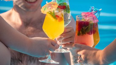 Bir grup insan havuzda eğleniyor, renkli kokteyllerle kadeh kaldırıyorlar. İçecekler taze meyve ve mini şemsiyelerle süslenir, eğlenceli ve ferahlatıcı atmosferi yakalar.