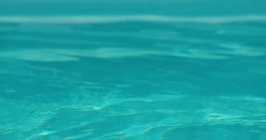 Arka planda havuzun berrak mavi suyu olan ferahlatıcı içeceklerle dolu bardakları tokuşturan yakın plan bir el. Sahne, sıcak bir yaz için mükemmel olan şenlikli ve serinletici havayı yakalar.