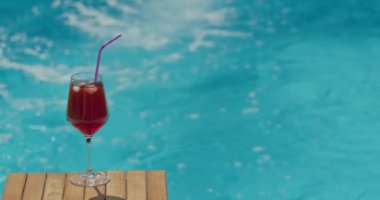 Soğuk bir kokteyl ile dolu bir bardak havuz suyu yüzeyinin arka planına kurulur. Parlak güneş ışığı sudan yansıyarak içeceğin canlı renklerini yükseltir ve bir...