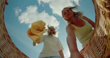 Sepetin içindeki perspektiften çamaşırları çıkarırken gülümseyen bir kadın ve bir çocuğun yer aldığı neşeli bir sahne. Gülüşleri ve neşeli ifadeleri,