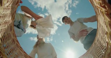 Bir aile çamaşır sepetine çarşaf atmak için birlikte çalışır. Sepetin içinden çekilen perspektifle birlikte. Arkaplanda kabarık bulutları olan güzel bir gökyüzü var.