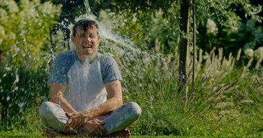 Çimenlerde bağdaş kurmuş bir adam aniden canlı bir bahçede suyla sırılsıklam olur. Onun şaşkınlık ve eğlence ifadesi ferahlatıcı anı yakalar. Etrafı yeşillik ve çiçeklerle çevrili.