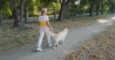 Aktif, yaşlı bir kadın güzel bir parkta Golden Retriever 'ıyla sakin bir yürüyüş yapıyor. Sahne sağlıklı ve aktif bir yaşam tarzını yansıtıyor. Formda kalmanın önemini vurguluyor.