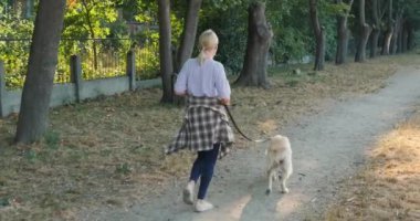 Orta yaşlı bir kadın dingin bir parkta Golden Retriever 'ıyla birlikte koşuyor, ikisi de temiz havanın ve yeşilliğin tadını çıkarıyor. Sadık köpeği yanında mutlu bir şekilde koşarken, kadın tempoyu sabit tutuyor.