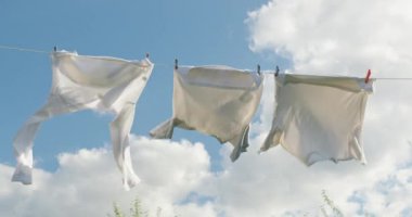 Üç beyaz gömlek temiz bir çamaşır ipinde asılı güneşli bir günde hafifçe rüzgarda hareket ediyorlar. Yumuşak bulutlarla kaplı canlı mavi gökyüzü, barışçıl ve temiz bir atmosfer yaratır.