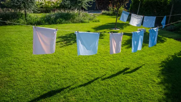 Stock image Pillowcases in soft pastel shades are neatly clipped to a clothesline, gently drying under the warm sun in a well-tended backyard. The green lawn below and the serene garden surrounding the scene