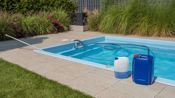 На этом снимке показана установка у бассейна, где два больших химических контейнера сидят возле бассейна с плавающим на воде моющим шлангом. Набор для тестирования воды стоит на краю бассейна,
