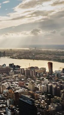 Sahne, nehrin üzerine altın bir parıltı saçarak sakin ve resimli bir atmosfer oluşturan güneş ışığının çarpıcı etkisini yakalıyor. Ön planda, New York 'un yüksek gökdelenleri