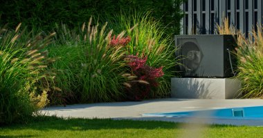 Açık hava ısı pompası, yemyeşil ve canlı çiçeklerle çevrili bir arka bahçe havuzunun yanında konumlandırılmıştır. Bu düzen, modern, sürdürülebilir, çevre dostu teknolojinin bir örneği.