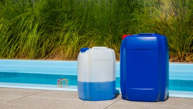 Bir havuz kenarı manzarası, suya batırılmış bir temizlik hortumuyla donatılmış bir havuz yanında iki büyük kap havuz kimyasalı içerir. Ayrıca havuz kenarında bir su test kiti de görülebilir.