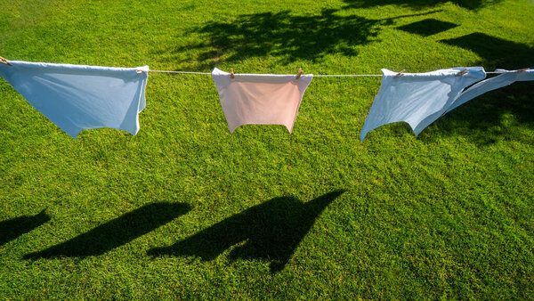 Pillowcases in vibrant colors sway gently on clotheslines above a lush, well-manicured lawn in a picturesque backyard. The peaceful setting, highlighted by the neat green grass, captures the simple