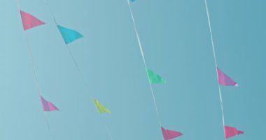 Parlak renkli parlak bayraklar açık mavi bir gökyüzüne asılmış güneş ışıl ışıl parlıyor. Bayraklar, yeşil, mavi ve sarı tonlarında, hafif bir esintide dalgalanıyor,