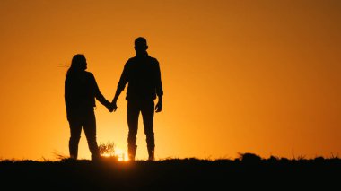 Romantik bir çiftin siluetleri. El ele tutuşmak ve güzel bir gün batımının arka planında durmak.