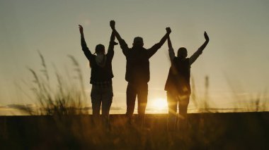 Batan güneşin arkaplanına karşı, çiftçi bir aile tarlalarında ayakta dururken başarılarının göstergesi olarak ellerini kaldırır.