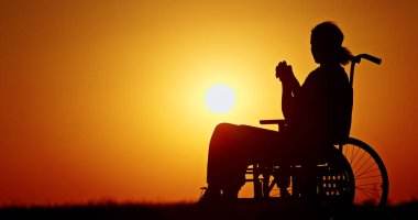 Gün batımında tekerlekli sandalyedeki bir insanın silueti huzurlu bir anı yansıtıyor. 