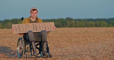 Çorak bir arazide tekerlekli sandalyede oturan bir adam elinde 