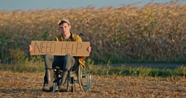 Çorak bir arazide tekerlekli sandalyede oturan bir adam elinde 
