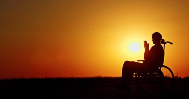Tekerlekli sandalyedeki bir insan canlı bir günbatımına karşı silueti ile sımsıkı sarılmış ve sakin bir şekilde yansıtılır. Batan güneşin altın rengi gökyüzünü dolduruyor, huzurlu ve huzurlu bir hava yaratıyor.