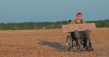 Çorak bir arazide tekerlekli sandalyede oturan bir adam elinde 