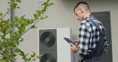 Bir teknisyen evin dışındaki ısı pompası ayarlarını ayarlamak için bir tablet kullanır.. 