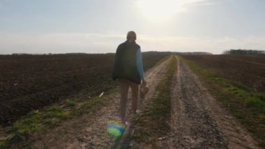 Bir kadın çiftçi tarlaların arasında köy yolunda yürüyor..