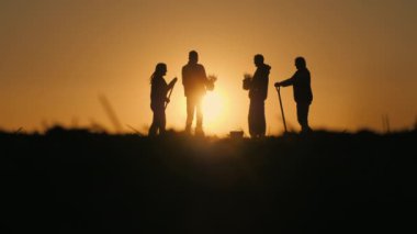 Tarladaki genç çiftçilerin siluetleri. Güneşin doğduğu, sohbet ettiği turuncu bir gökyüzüne karşı duruyorum..