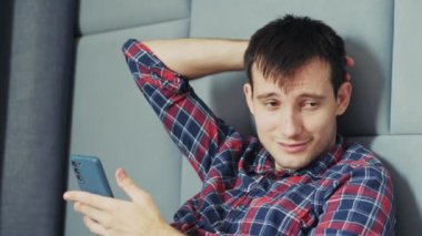 Üzgün bir adam elinde akıllı telefonuyla bir yatakta oturur, başının arkasını kaşır ve kötü haber aldıktan sonra ağlamak üzeredir. Yüksek kalite 4k görüntü