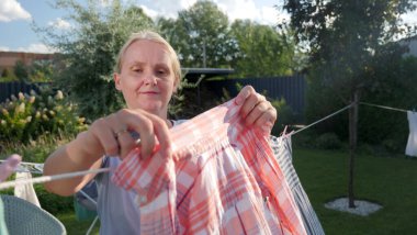 Woman hanging a checkered shirt on a clothesline in a sunny backyard, smiling with satisfaction. High quality photo clipart