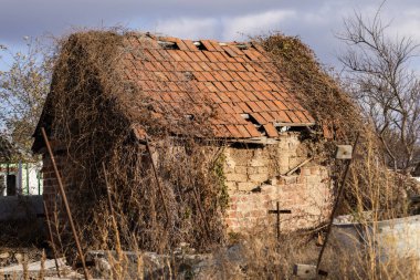 Kuru bitki örtüsü ve ihmal belirtileriyle çevrili döşeme kiremitli çatılı eski bir kır evi. Yüksek kalite fotoğraf