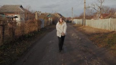 Genç bir kadın, köhne tek katlı evlerle çevrili çamurlu bir sokakta yürüyor. Soğukta titriyor ve ellerini ısıtmaya çalışıyor.