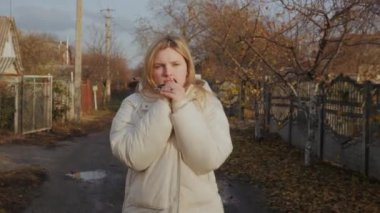 Genç bir kadın çamurlu bir sokakta yürüyor. Etrafı köhne, tek katlı evlerle çevrili ve ellerini ısıtmaya çalışıyor. 