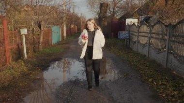Çamurlu bir yolda çamurlu bir yolda yürüyen, cep telefonuyla konuşan, yoksul bir topluluktaki harap olmuş evlerle çevrili bir kadın. Yüksek kalite 4k görüntü