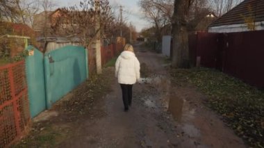 Genç bir kadın çamurlu toprak bir yolda yürüyor. Çırpınan bir mahalledeki harap evlerle kaplı, kalın bir ceket giymiş.