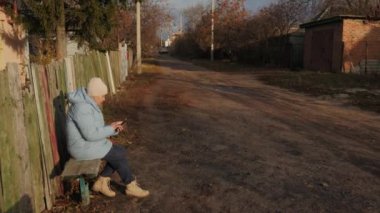Ukrayna 'nın kırsal kesiminde ahşap bir çitin kenarında sakin bir günde cep telefonu kullanan son sınıf öğrencisi bir kadın. 