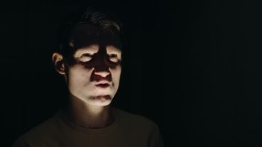 Dramatik ışıklandırmada genç bir adamın portresi, karanlık bir ortamda yüzüne gölgeler düşürüyor. Yüksek kalite 4k görüntü