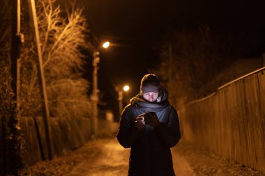 Gece sessiz bir yolda yürürken el ele tutuşan çift, çıplak ağaçlar ve sakin bir atmosferle çevrili bir sokak lambasıyla aydınlatılıyor. Yüksek kalite fotoğraf