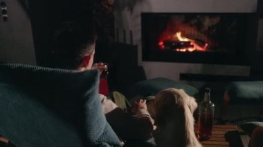 Şöminedeki ateşe bakan genç adam, elinde bir bardak viskiyle, yanında rahat bir ortamda Golden Retriever 'ıyla oturuyor. Yüksek kalite 4k görüntü