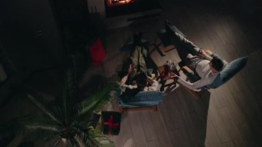 Şöminenin yanında hediye kutusuyla rahatlayan iki adam ve neşeli bir köpek etrafta koşuşturuyor, keyifli bir bayram akşamının tadını çıkarıyorlar. Yüksek kalite 4k görüntü
