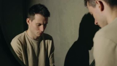 Genç adam ellerini ve yüzünü aynanın önünde yıkıyor, karanlıkta spot ışıklarıyla aydınlatılıyor, gölgesi duvarda, çok yorgun görünüyor. Yüksek kalite 4k görüntü