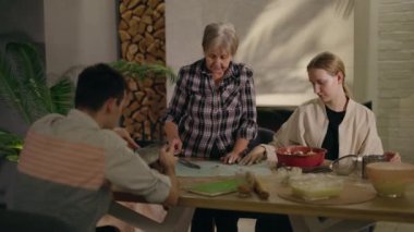 Son sınıf öğrencisi bir kadın ve iki torunu mutfakta birlikte pizza hazırlıyorlar, şöminenin yanında. Aile neşe ve neşe dolu anları paylaşır, heyecan ve beklentiyle