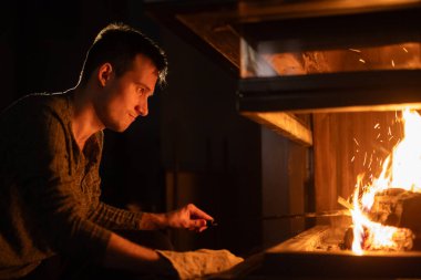 A young man carefully tends to a fireplace, adjusting the flames with a poker. The warm glow of the fire illuminates his face, creating a cozy and focused atmosphere. High quality photo clipart