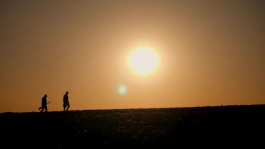 Güneşin doğuşunda ya da batışında, parlayan güneşe karşı gölgeli bir tarlada yürüyen iki çiftçi. Sahne, kırsal hayattaki basitliği ve doğayla olan bağlantıyı vurguluyor. 