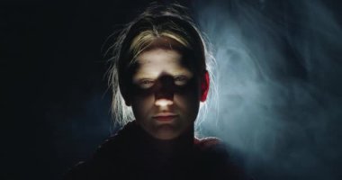 Karanlıktaki genç bir kızın rahatsız edici portresi. Derin gölgeli dramatik ışıkla aydınlatılmış. Korku ve gizem kavramını çağrıştırıyor. Yüksek kalite 4k görüntü