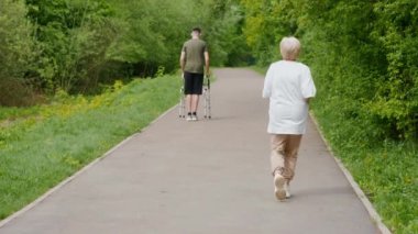 Yaşlı bir kadın ve genç bir adam yemyeşil bir parkta neşe içinde yürüyorlar, sağlık ve sağlık yararlarını destekliyorlar.