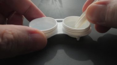 Kontakt lens kutusunun aşırı yakın çekimi, elinde cımbızla bir lensi nazikçe çıkarıyor.