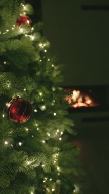 Güzel dekore edilmiş bir Noel ağacı, kırmızı süslemeleri ve parıldayan ışıklarıyla, rahat bir oturma odasında, arka planda parlayan bir şömineyle.