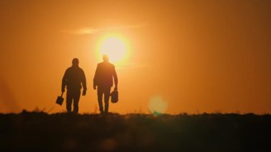  Ateşli bir günbatımı gökyüzüne karşı siluet oluşturan iki çiftçi, kırsal bir alanda birlikte yürüyorlar, tarım işleri için gerekli aletleri taşıyorlar, çiftçilik hayatındaki adanmışlık ve takım çalışmasını somutlaştırıyorlar. 