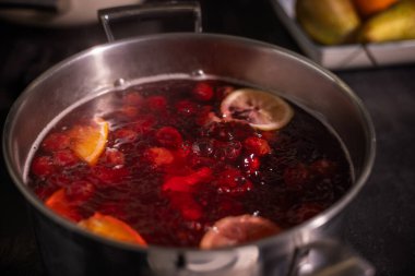 Kaynayan kırmızı meyve kompostosu, portakal dilimleri, limon dilimleri ve canlı meyvelerle dolu bir tencere sıcak ve davetkâr bir yemek sahnesi yaratıyor. Yüksek kalite fotoğraf