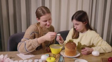 İki kız festival malzemeleriyle dolu bir masada Paskalya pastasını süslüyorlar yaratıcılık ve aile gelenekleri sergiliyorlar. Yüksek kalite 4k görüntü